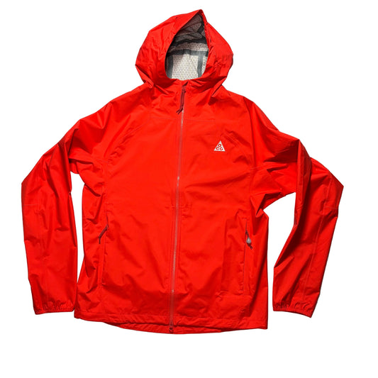 A bright red hooded windbreaker jacket laid flat on a white surface. The jacket features a full front zipper, zippered hand pockets, and a small white ACG logo on the left chest.