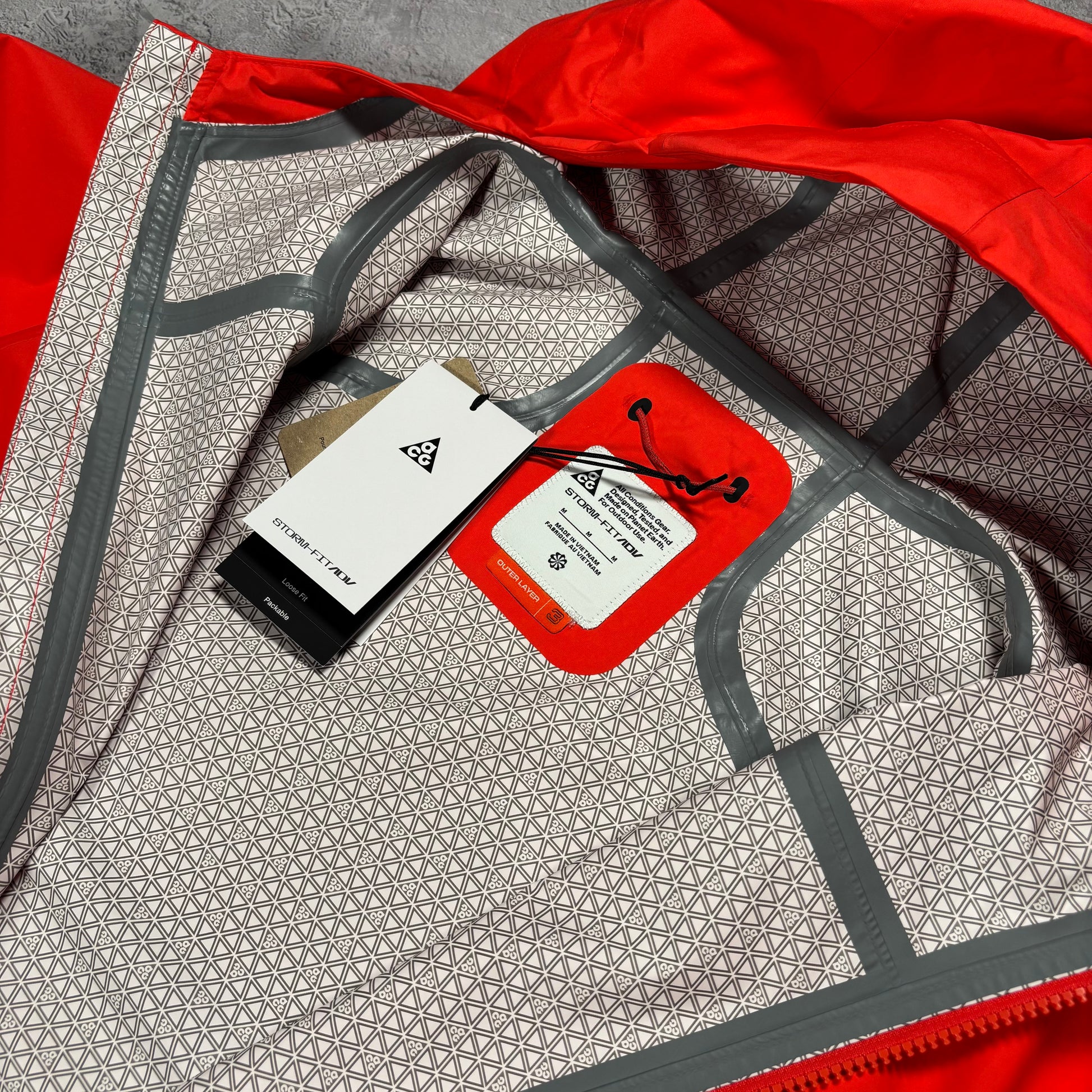 Close-up of the inside of a red jacket or garment showing a patterned lining, gray trim, and two hang tags attached near the collar area.
