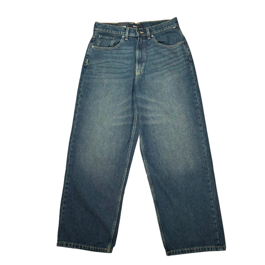 A pair of worn wash dark blue denim jeans laid flat on a white surface.