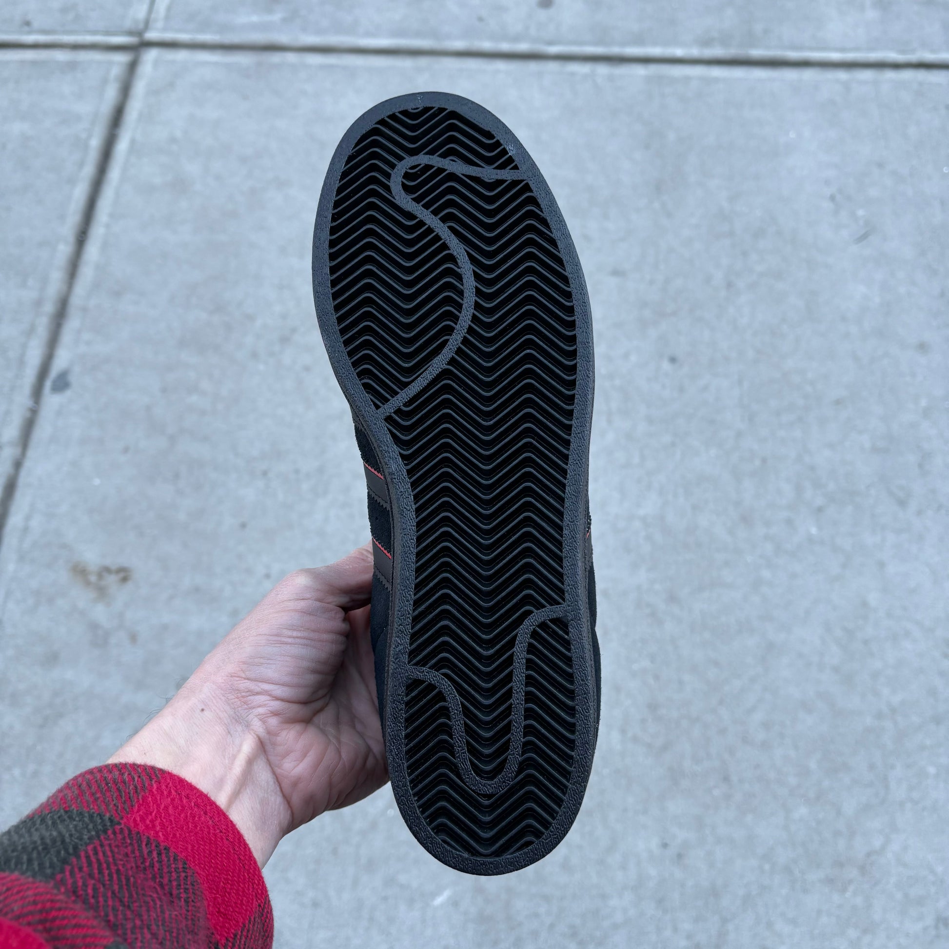 view of outsole of black, red and gold suede skateboard sneaker