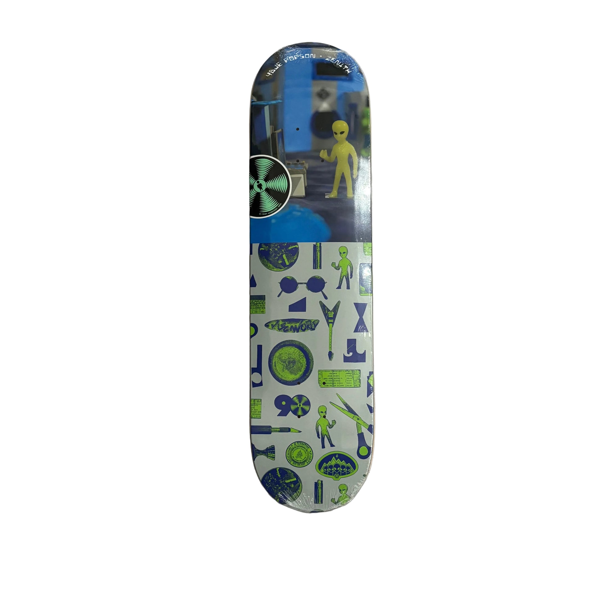 A skateboard deck with a graphic alien-themed design, featuring a yellow alien on a blue background on the top half and green and blue sci-fi icons on a white background on the bottom half, displayed on a white surface.