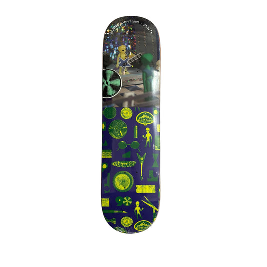 A skateboard deck with a dark blue and green alien-themed graphic design, photographed flat on a white surface.