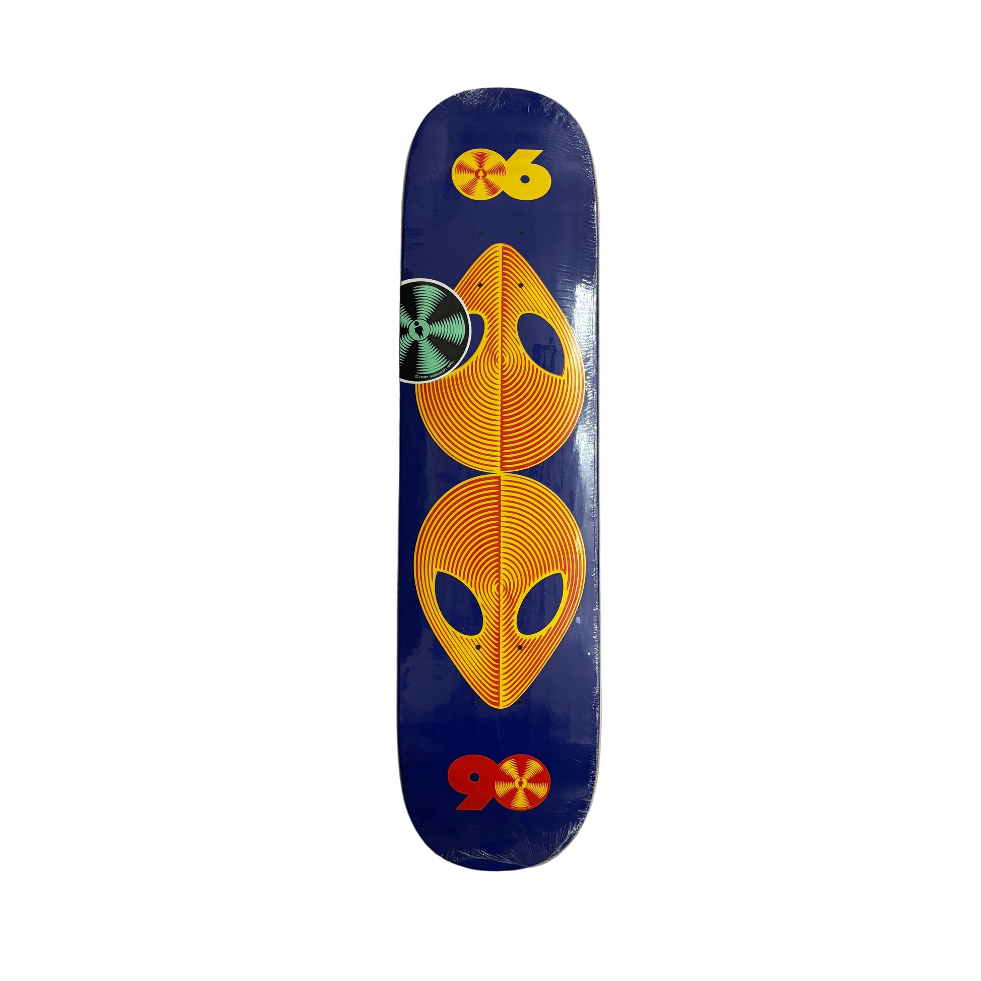 A skateboard deck with a dark blue background and a symmetrical alien-themed graphic in orange, yellow, and green, photographed from directly above on a white surface.