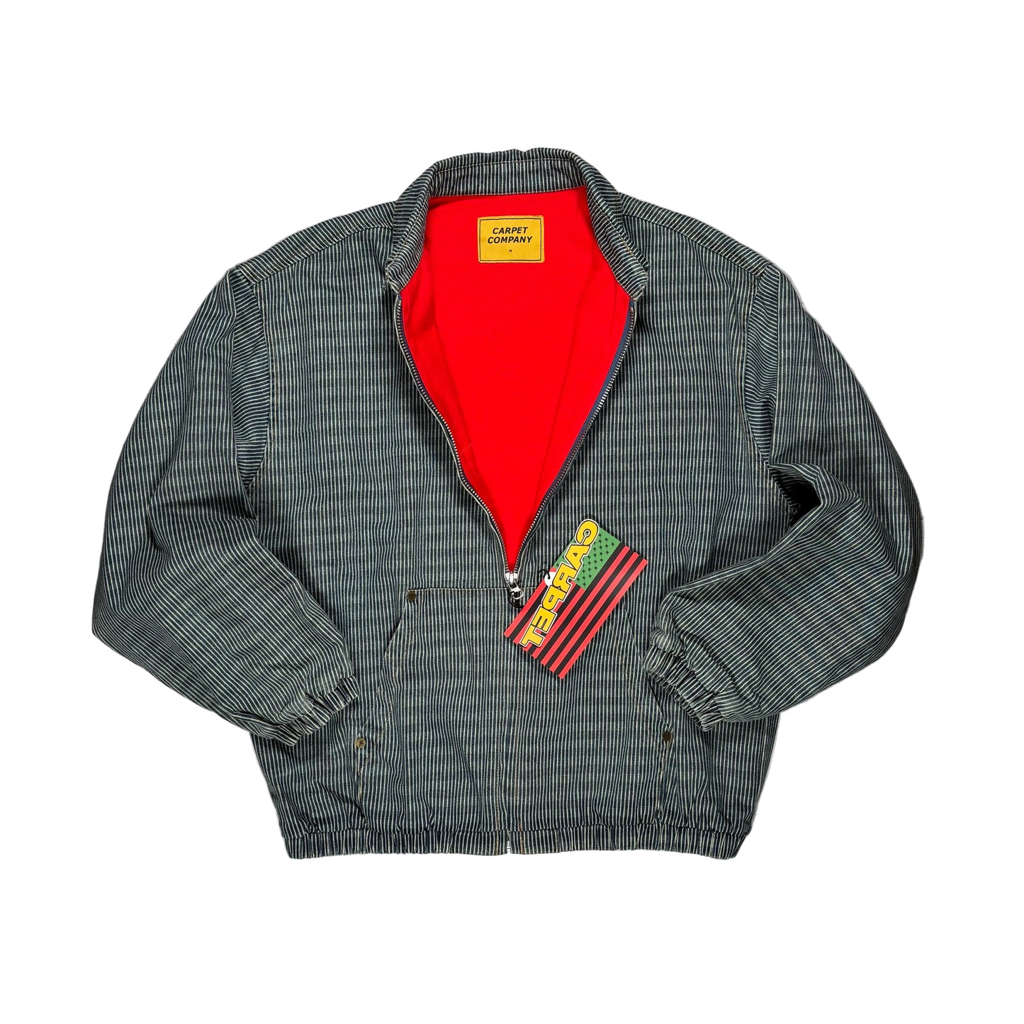 A vintage Carhartt jacket laid flat on a textured gray background, featuring a gray and black pinstripe pattern, a bright red interior lining, and a yellow Carpet Company label below the collar.