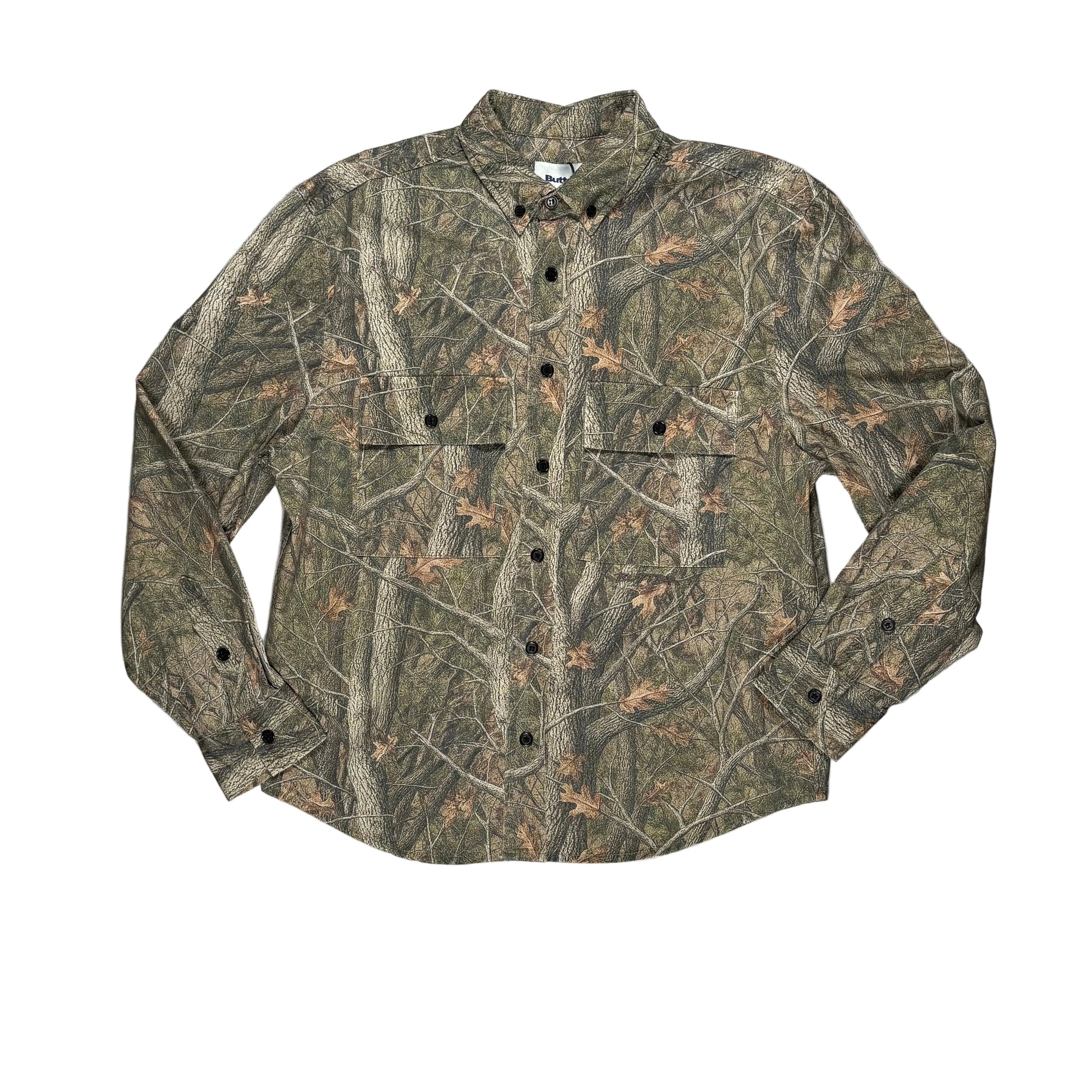 A long-sleeve button-up shirt with a woodland camouflage pattern, black buttons, laid flat on a white surface.