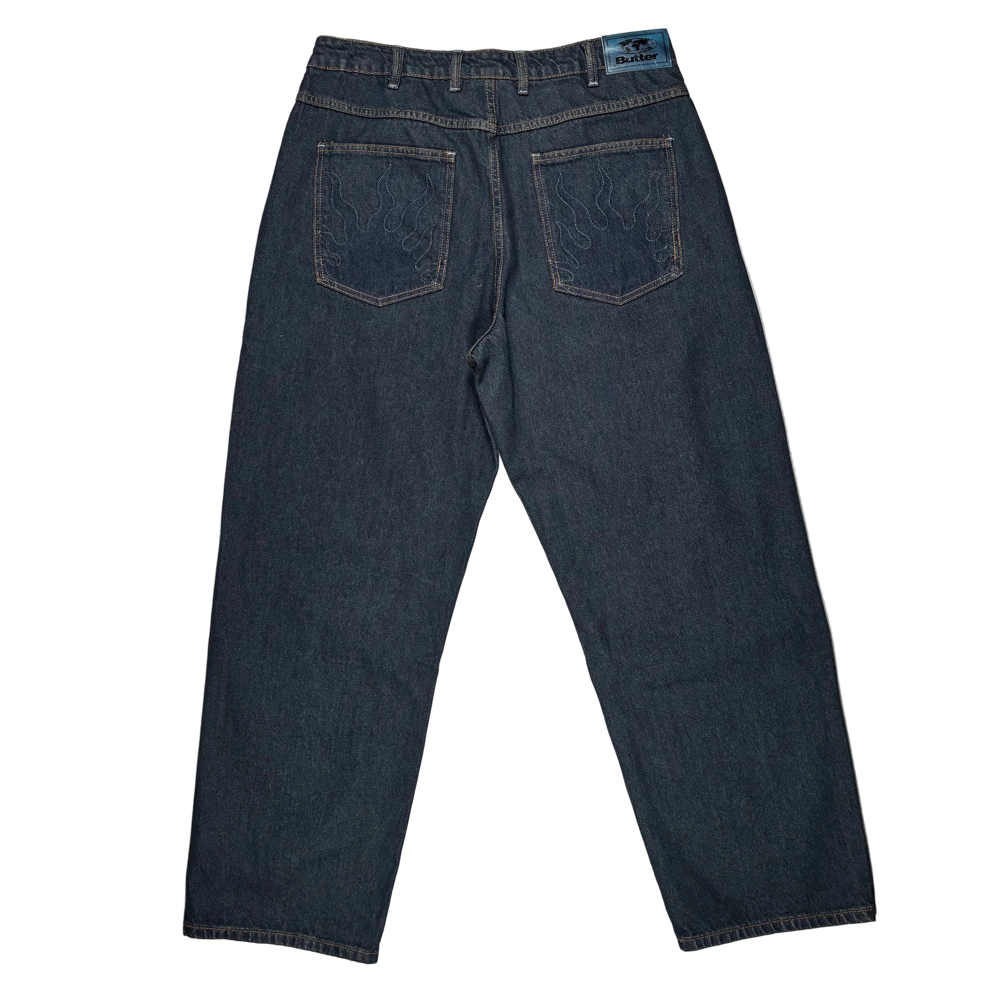 Back view of dark indigo denim jeans laid flat on a white surface, showing embroidered back pockets and a blue waistband label.