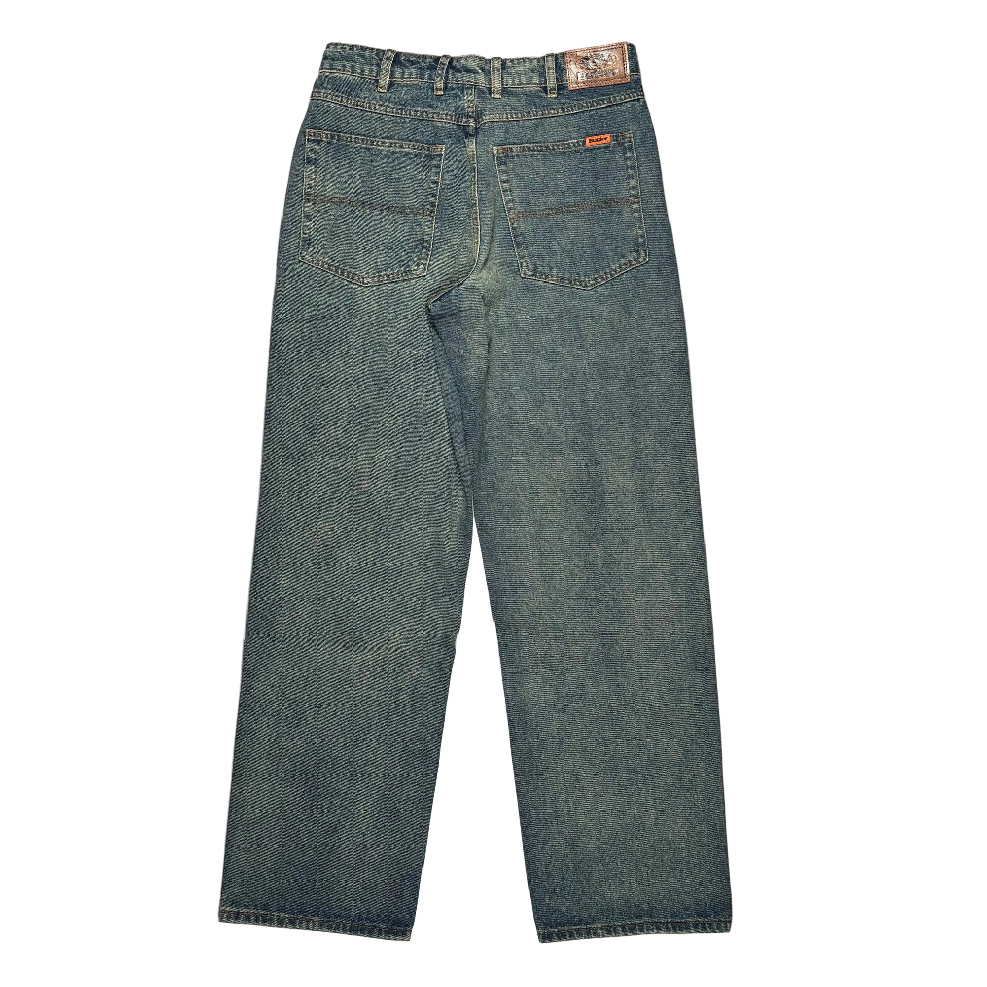 Back view of a pair of blue denim jeans laid flat on a white surface. Jeans have two back pockets with brown patch on waistband.