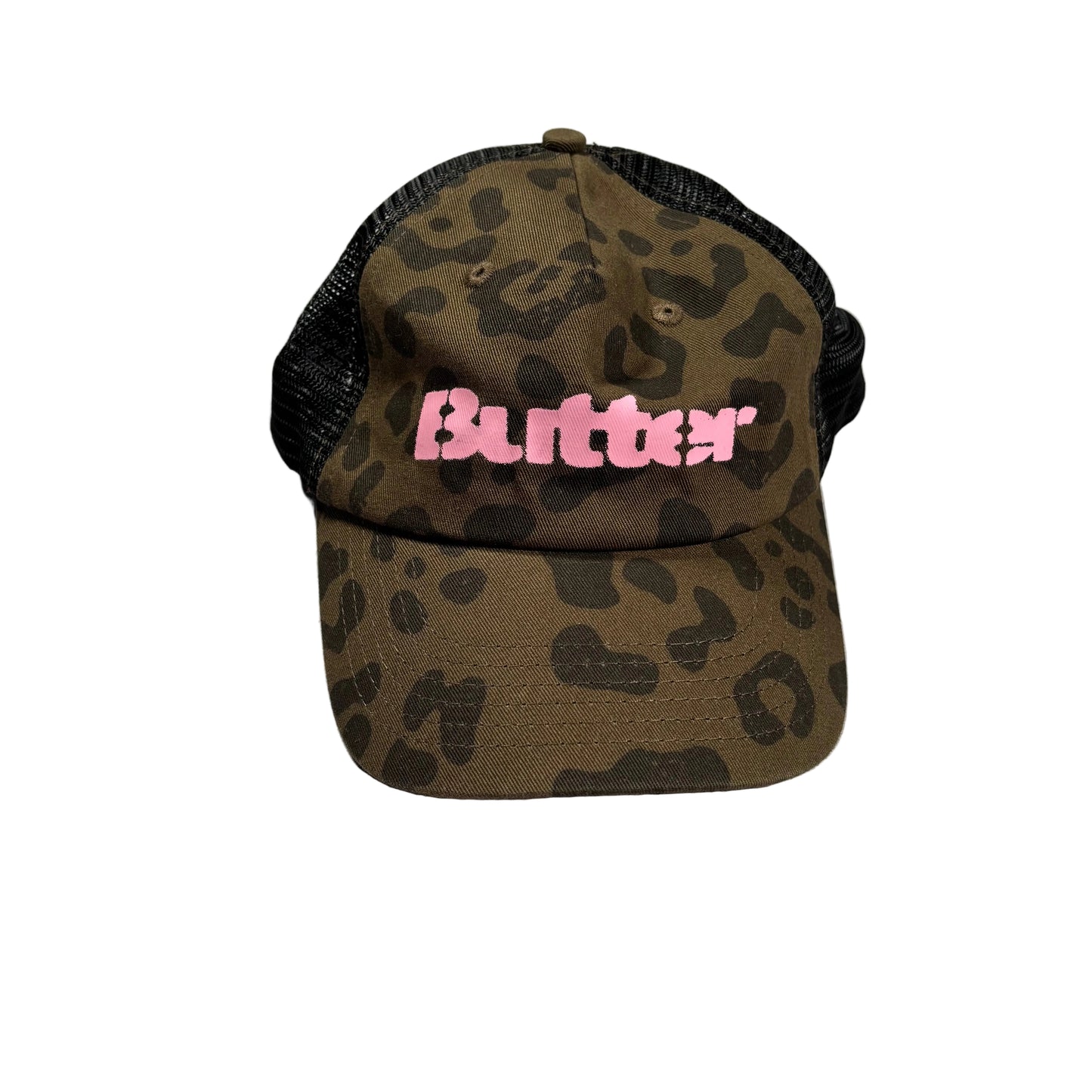 A trucker-style cap with a brown and black leopard print pattern on the front and brim, black mesh back panels, and a pink 'Butter' logo on the front, resting on a white surface.