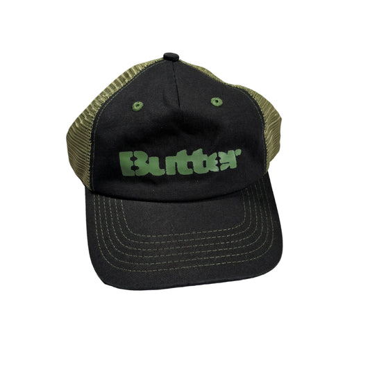 A black trucker hat with olive green mesh back panels and a green 'Butter' logo on the front, resting on a white surface.