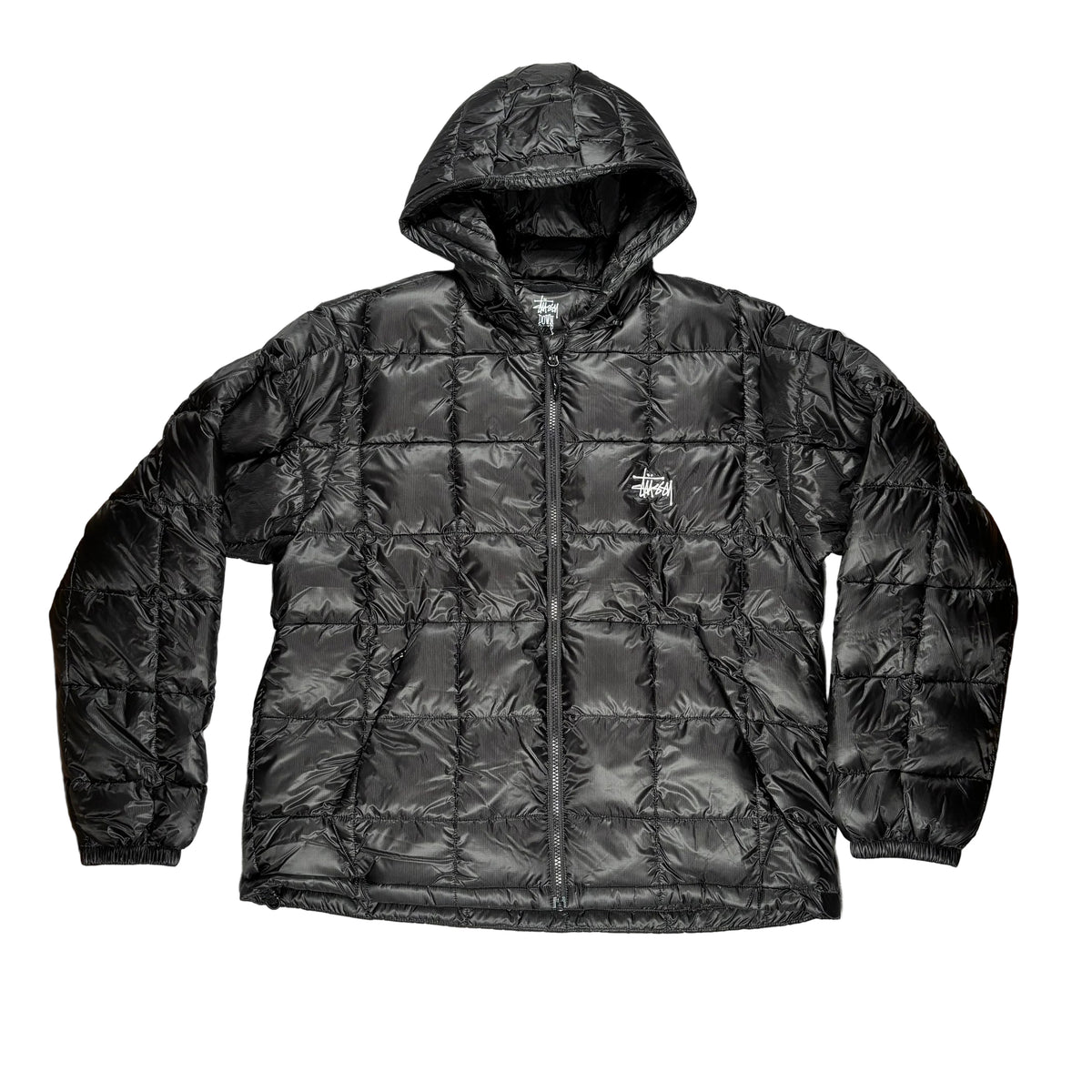 A black quilted puffer jacket with a hood and front zipper, laid flat on a white surface. A small Stussy logo is visible on the left chest.