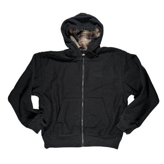 A black zip-up hoodie laid flat on a white surface. The hoodie features a small tonal embroidered logo on the left chest, a front zipper, and a hood with a plaid lining visible inside.