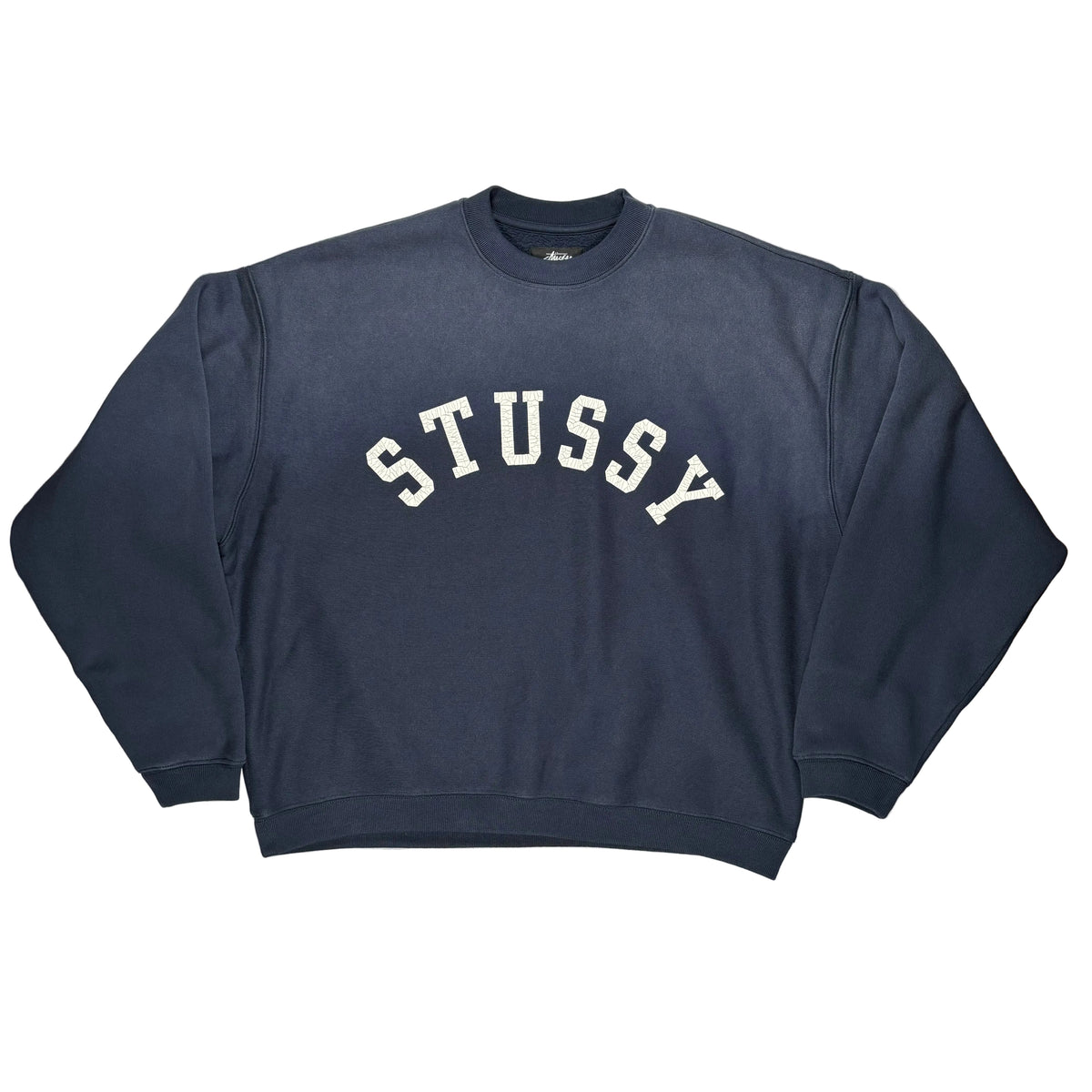 A navy blue Stussy crewneck sweatshirt with 'STUSSY' printed in white arched varsity letters across the chest, laid flat on a white surface.