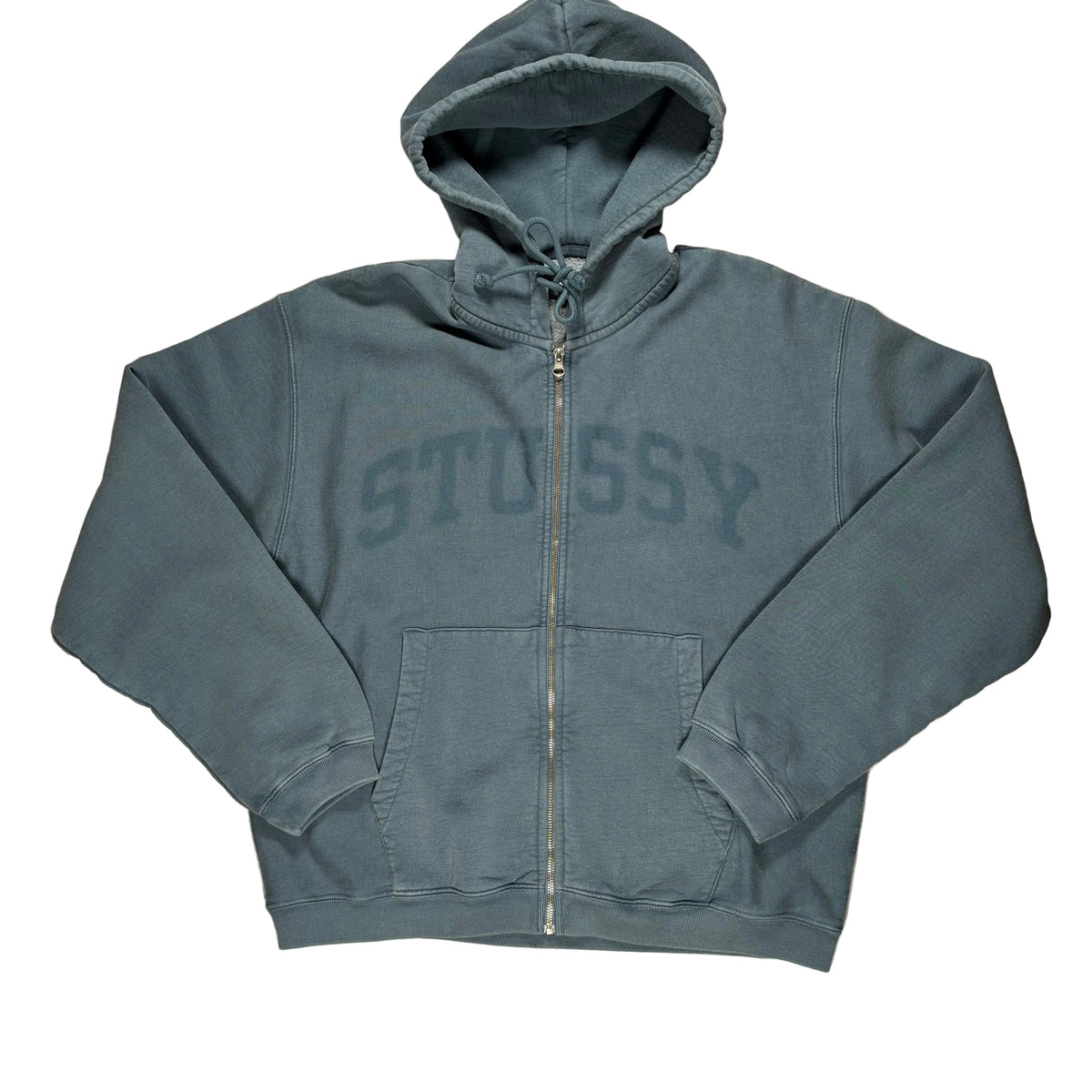 A slate washed navy zip-up hoodie with a large tonal 'Stussy' graphic printed horizontally  on the front, laid flat on a white surface.