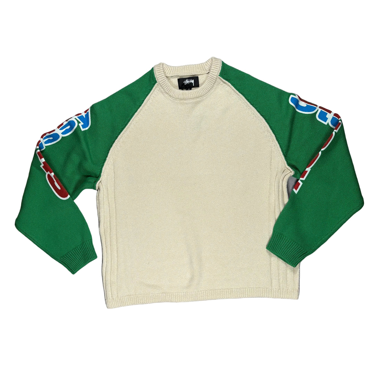 A Stussy crewneck sweater laid flat on a white surface, featuring a cream body and green raglan sleeves with colorful graphics.