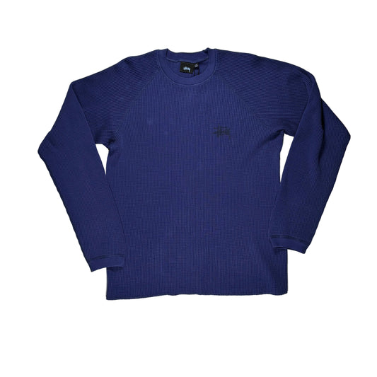 A navy blue ribbed long-sleeve crewneck shirt by Stüssy, laid flat on a white surface.