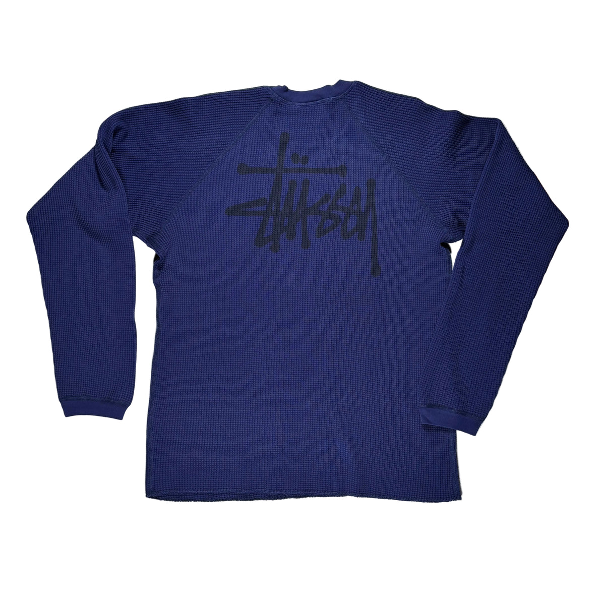 A navy blue ribbed long-sleeve shirt with a large black Stüssy logo printed across the back, laid flat on a white surface.
