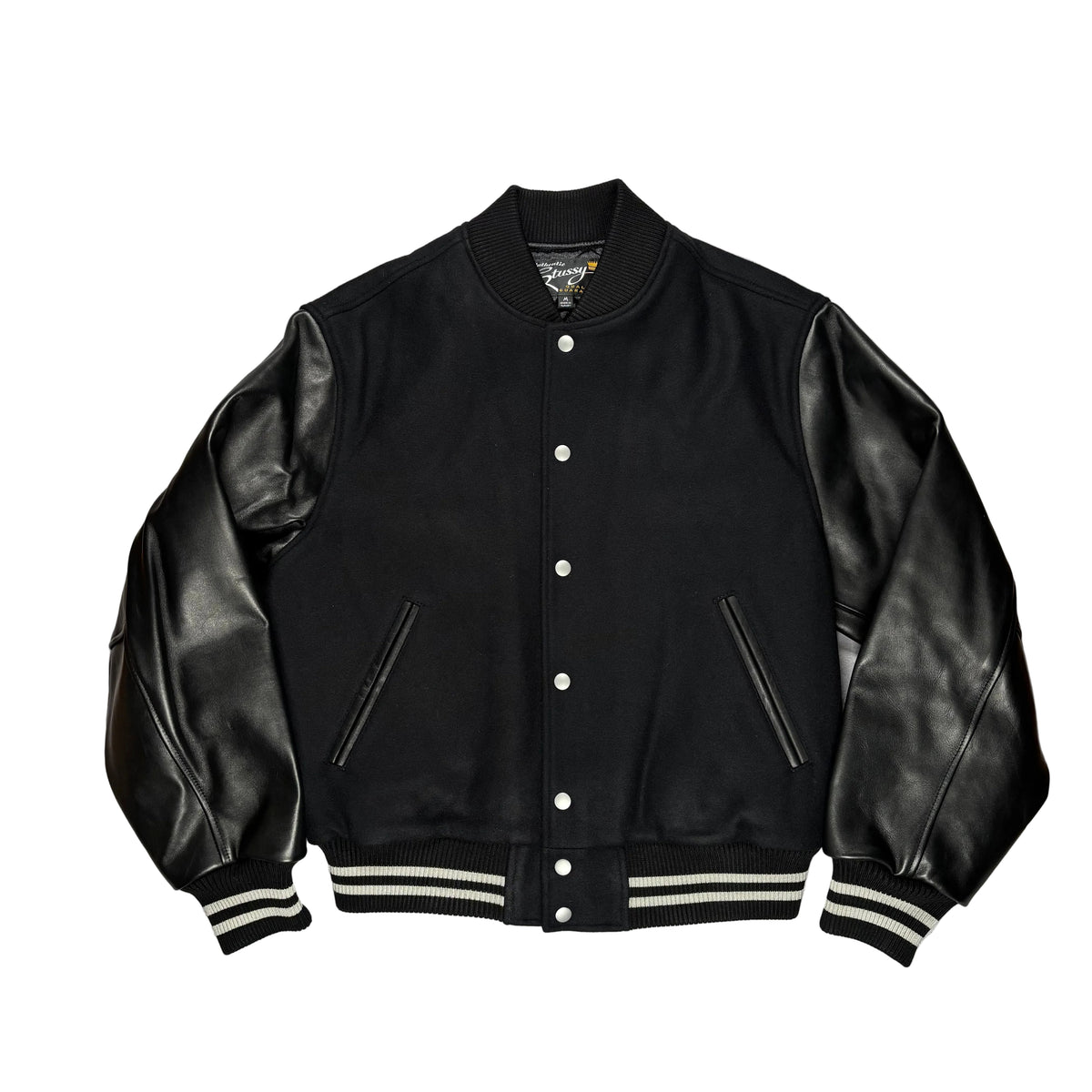 A black varsity-style jacket with smooth leather sleeves, ribbed knit collar, cuffs, and hem, and silver snap buttons, laid flat on a white surface.