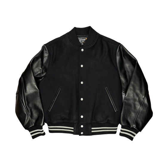A black varsity-style jacket with smooth leather sleeves, ribbed knit collar, cuffs, and hem, and silver snap buttons, laid flat on a white surface.