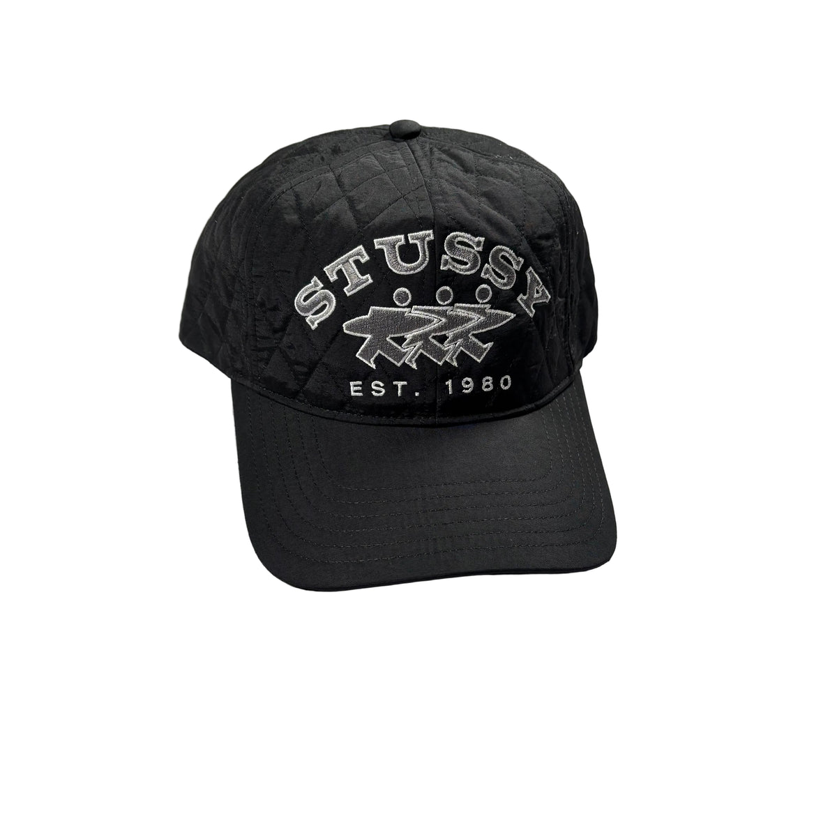 A black quilted Stussy baseball cap with white embroidered lettering and logo, resting on a white surface.
