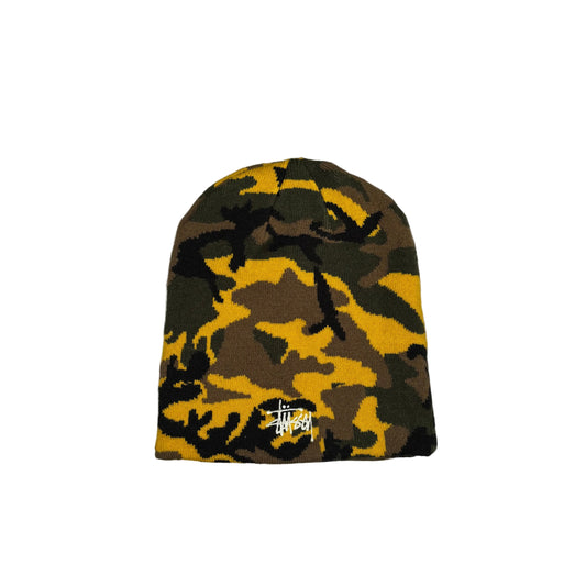 A Stüssy beanie hat featuring a yellow, brown, and black camouflage pattern, displayed flat against a white background.