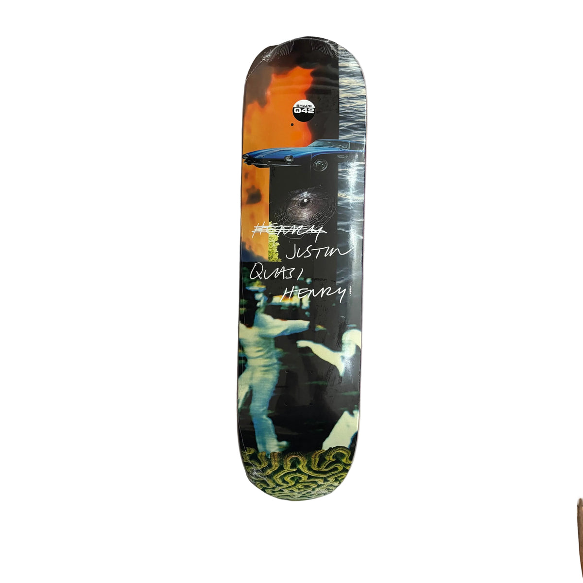 A skateboard deck with a complex collage graphic design, featuring a black and white photo of a figure, a blue car, and orange sky elements, resting on a white surface.