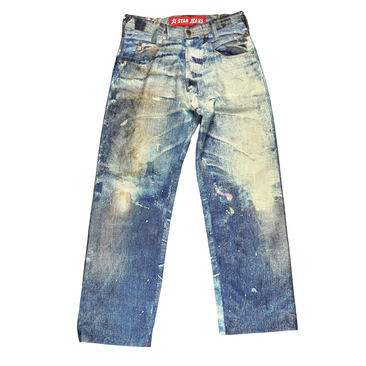 A pair of heavily distressed blue denim jeans laid flat on a white surface. The jeans feature extensive fading and paint-splatter style.