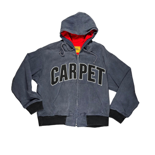 A charcoal gray zip-up hooded jacket with 'CARPET' printed across the chest in black varsity letters with a white outline. Featuring a red interior hood lining and black ribbed cuffs and hem, laid flat on a white.