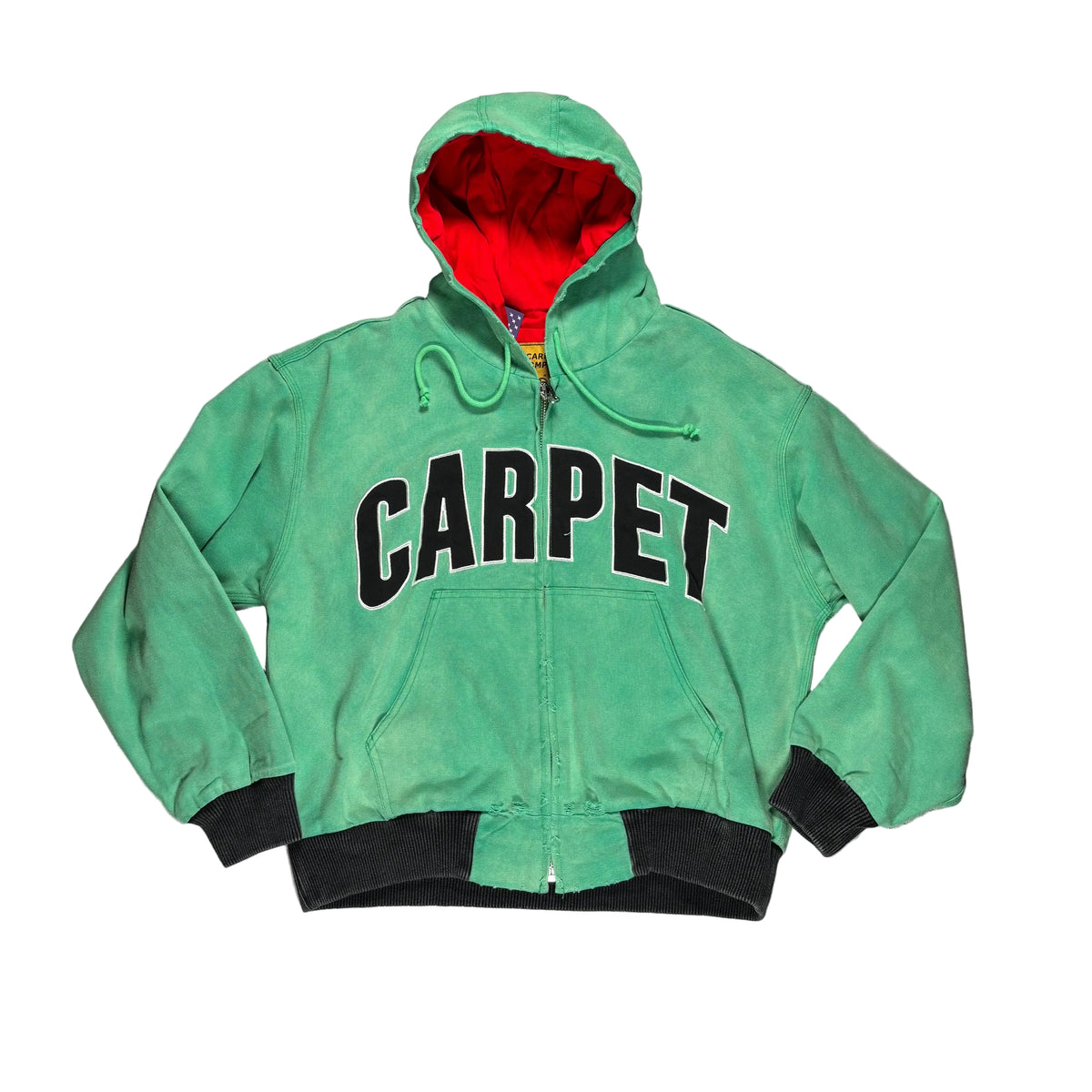 A green zip-up hooded jacket laid flat on a white surface, with a red hood lining and black trim. The front has large black 'CARPET' lettering outlined in white.
