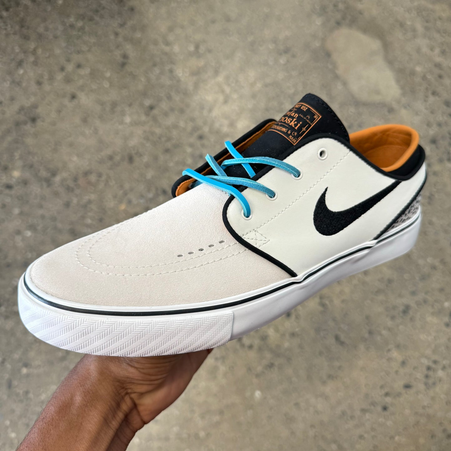 white suede shoe with blue laces and black accents and logo