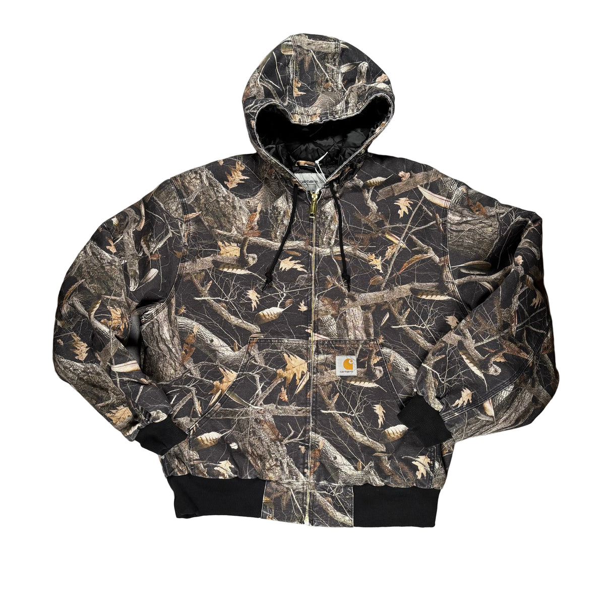 A Carhartt hooded jacket in a woodland camouflage print, laid flat on a white surface.