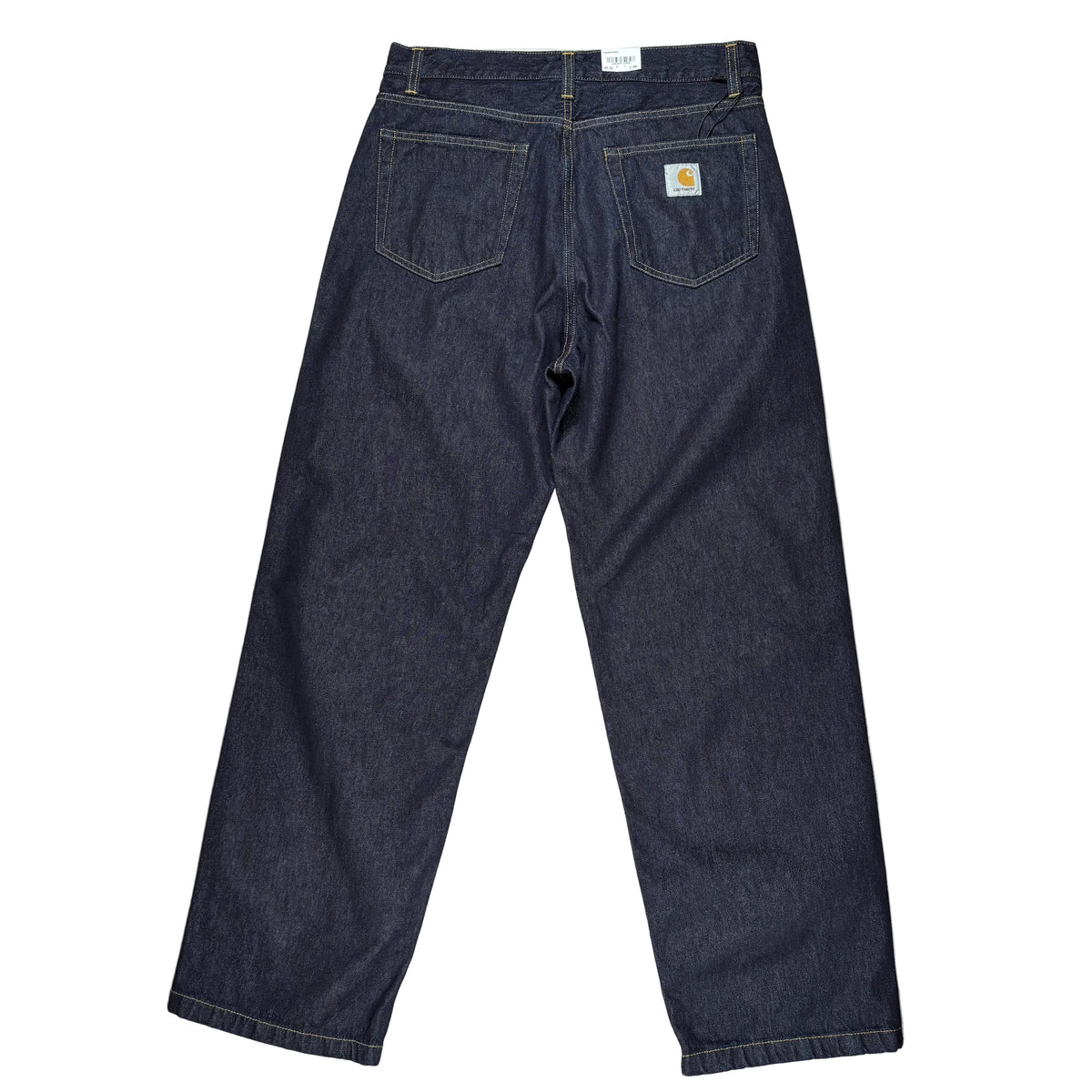 Back view of dark indigo denim jeans laid flat on a white surface. A small Carhartt logo patch is visible on the back pocket.