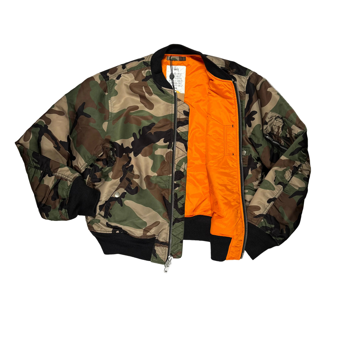 A bomber jacket laid flat on a white background, featuring a classic green, brown, and beige camouflage pattern on the exterior, a bright orange interior lining, and black ribbed trim on the bottom and cuffs.