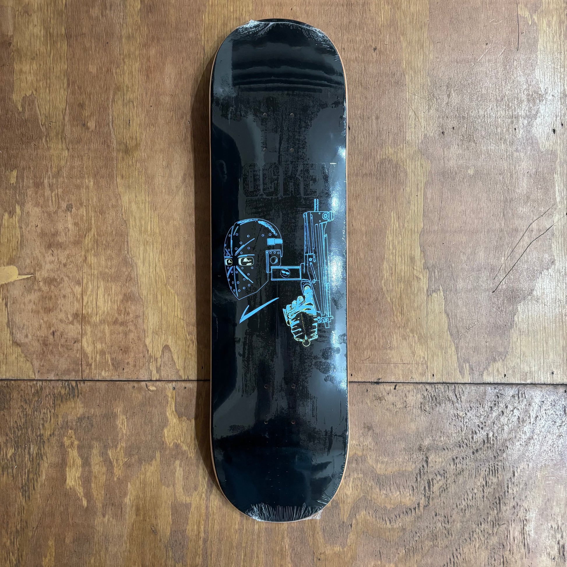 black deck with man in hockey mask holding a machine gun on center of skateboard deck