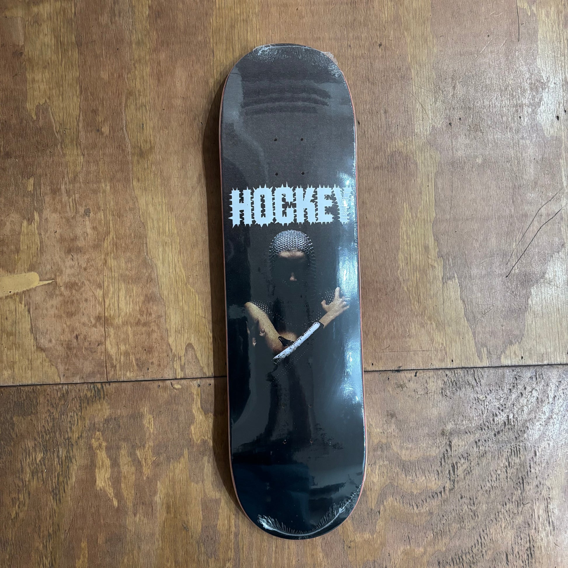 metal looking human showing off arms on black deck that reads HOCKEY