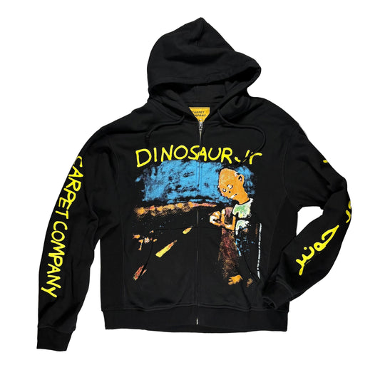 A black zip-up hoodie laid flat on a white surface. The hoodie has a large multicolor graphic on the front with yellow text reading 'DINOSAUR JR' and yellow vertical text on both sleeves reading 'CARPET COMPANY.