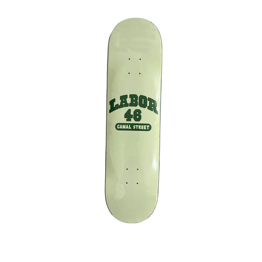A cream colored skateboard deck with dark green text reading 'LABOR 46 CANAL STREET' in the center, photographed from above on a white surface.