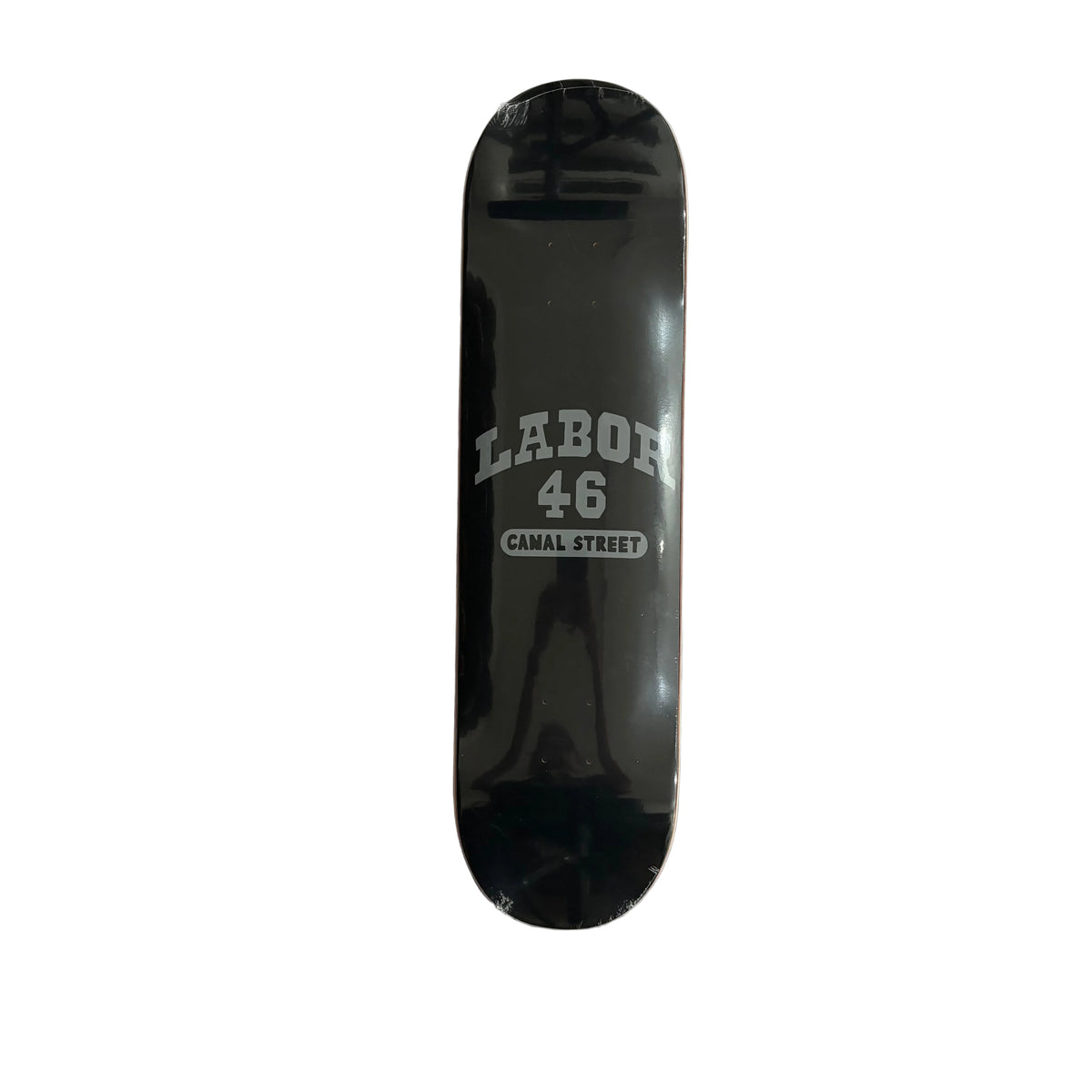 A black skateboard deck with 'LABOR 46 CANAL STREET' printed in grey, displayed on a white surface.