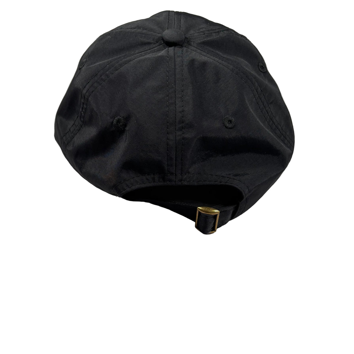 A black baseball cap viewed from the back, resting on a white surface. The cap features a black fabric crown with a central button, matching black eyelets, and a black adjustable strap with a small gold-tone metal buckle.