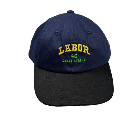 A navy blue baseball cap with a black visor, featuring yellow and green embroidered text reading 'LABOR 46 CANAL STREET' on the front, displayed on a white surface.