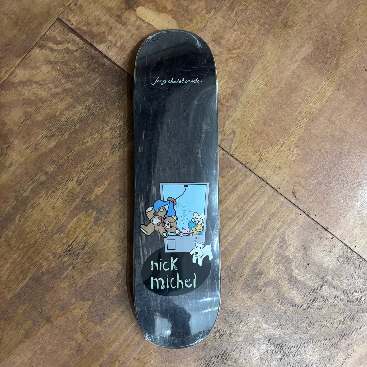 woodgrain skateboard deck with cartoon of claw machine game grabbing a teddy bear