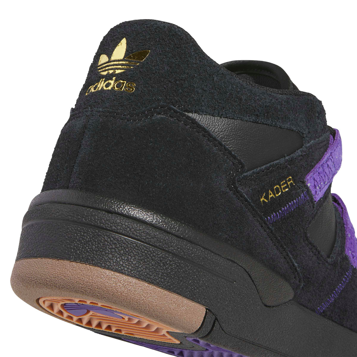 Close-up of a black Adidas Kader sneaker showing the heel, gold trefoil logo, purple accents, and gum outsole.
