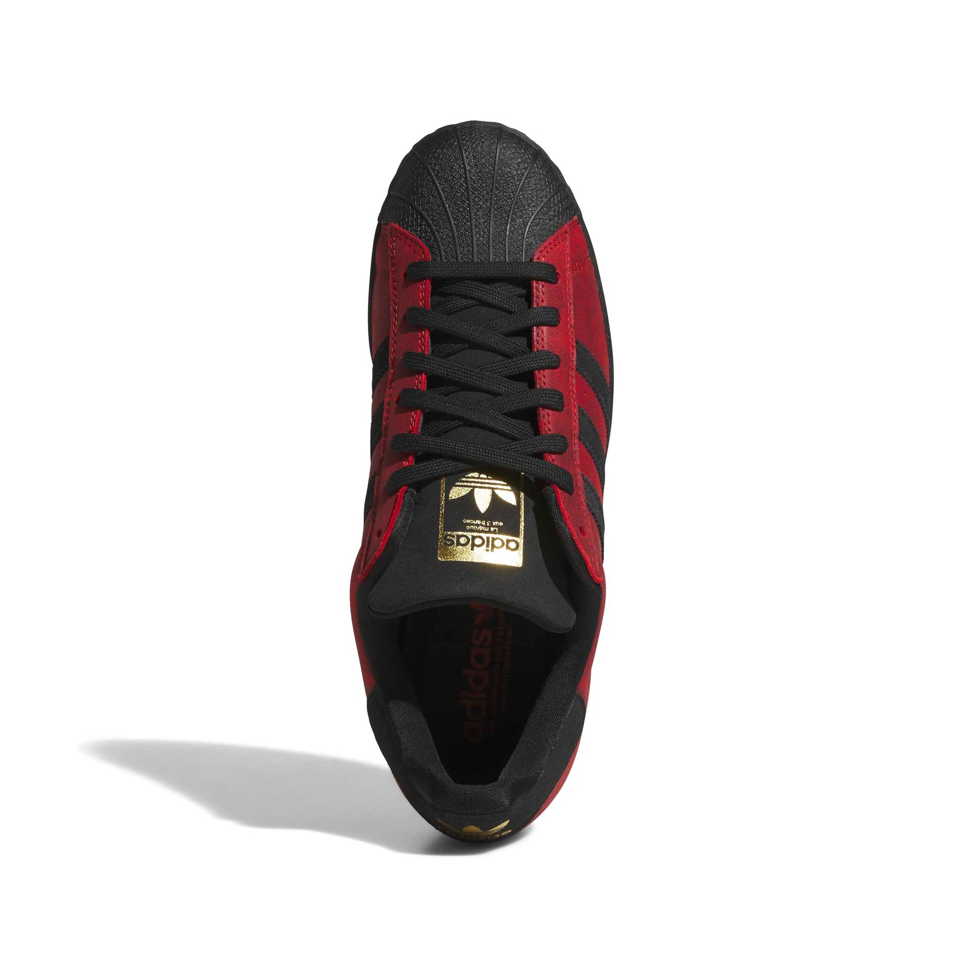 A single Adidas Superstar sneaker shown from a top-down view, featuring a black and red colorway with a metallic gold logo on the tongue.