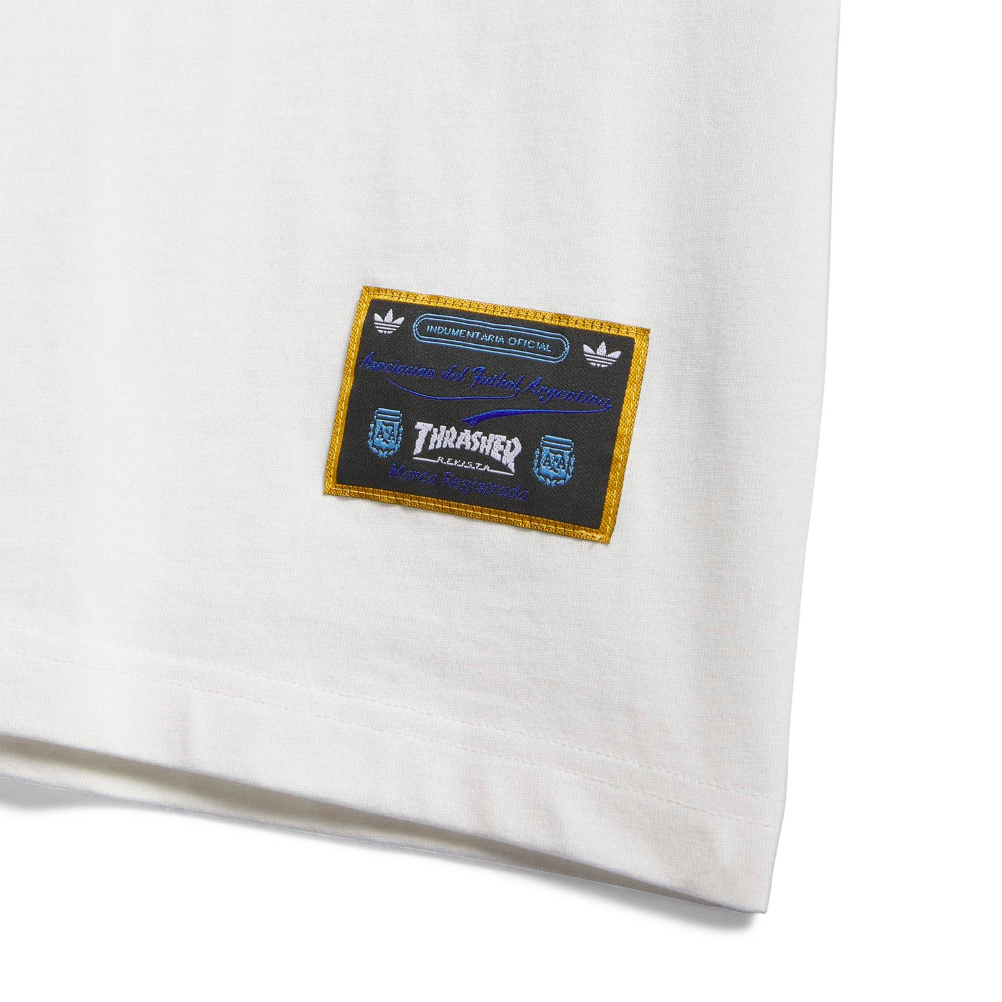 Close-up of a white t-shirt with a branded patch featuring Adidas and Thrasher logos.