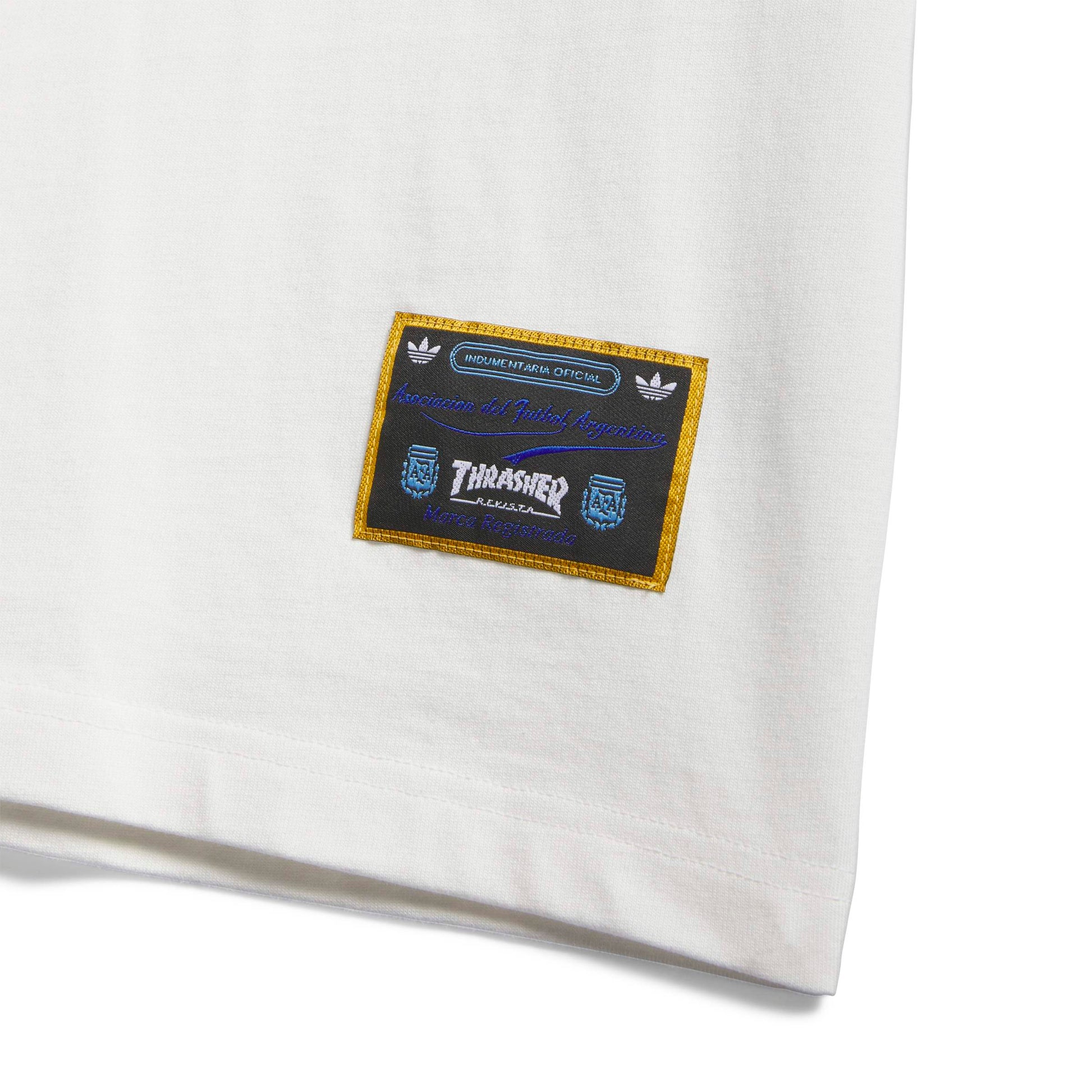 Close-up of a white t-shirt with a branded patch featuring Adidas and Thrasher logos.
