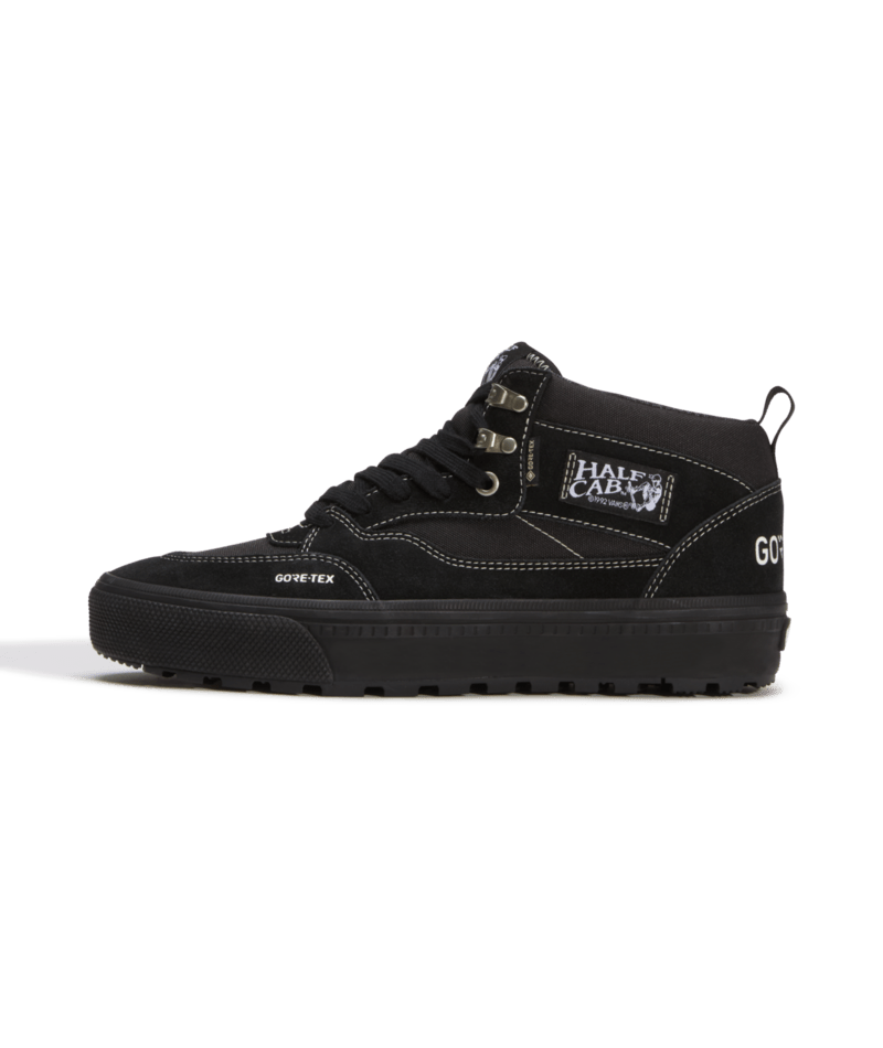A black mid-top sneaker from Half Cap x Vans, featuring a black suede and canvas upper, black laces, a black sole, and white contrast stitching. The side displays a 'HALF CAP X VANS' patch and 'GORE-TEX' branding.